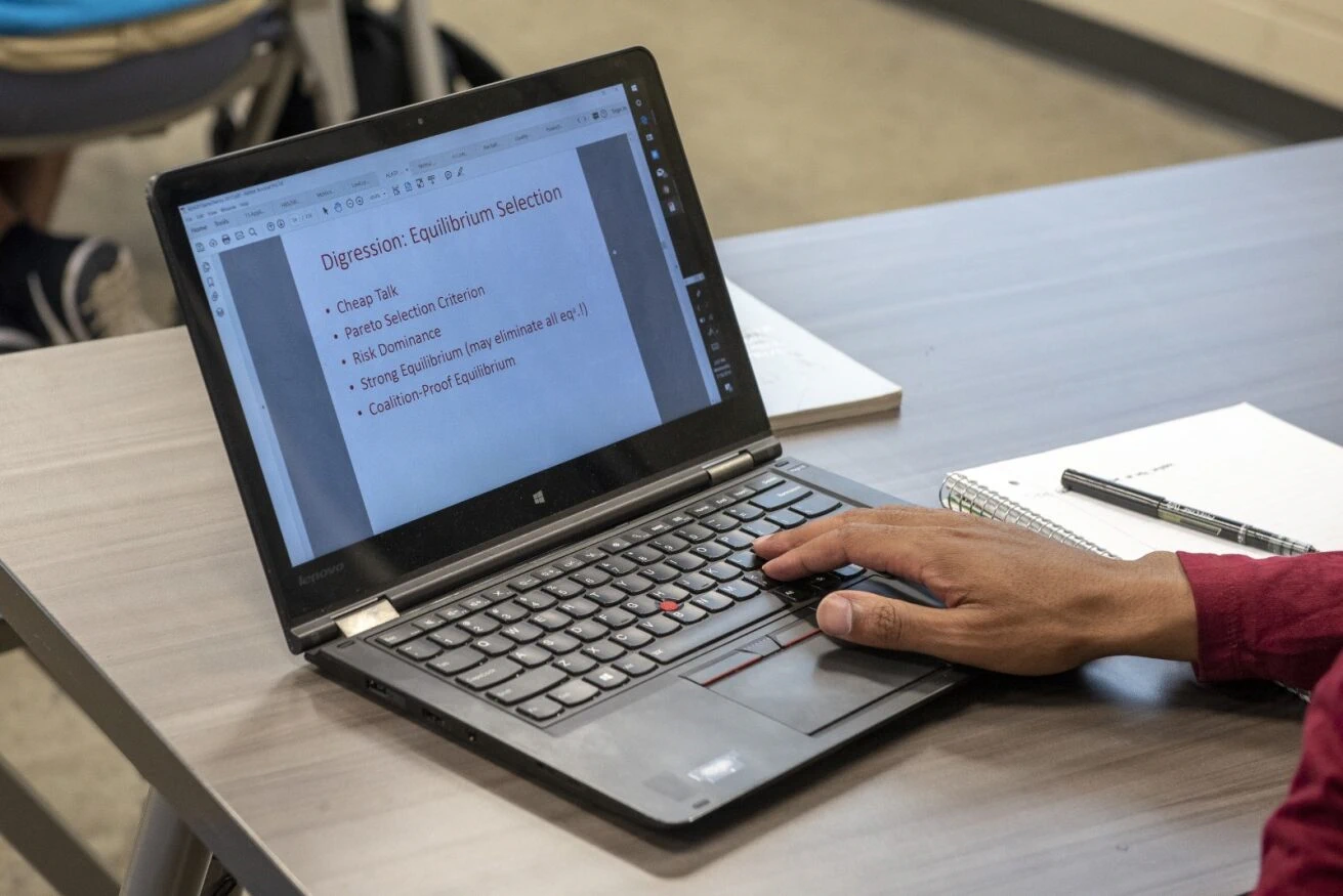 A laptop on a table with a brown hand typing. 