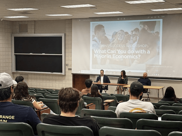 Two men and one woman in a lecture hall answering questions.